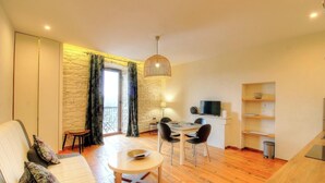 Un salon avec un canapé, une table à manger et des chaises, un téléviseur et un mur en pierre.