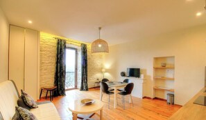 Ein Wohnzimmer mit einer Couch, einem Esstisch mit Stühlen, einem Fernseher und einer Steinwand.