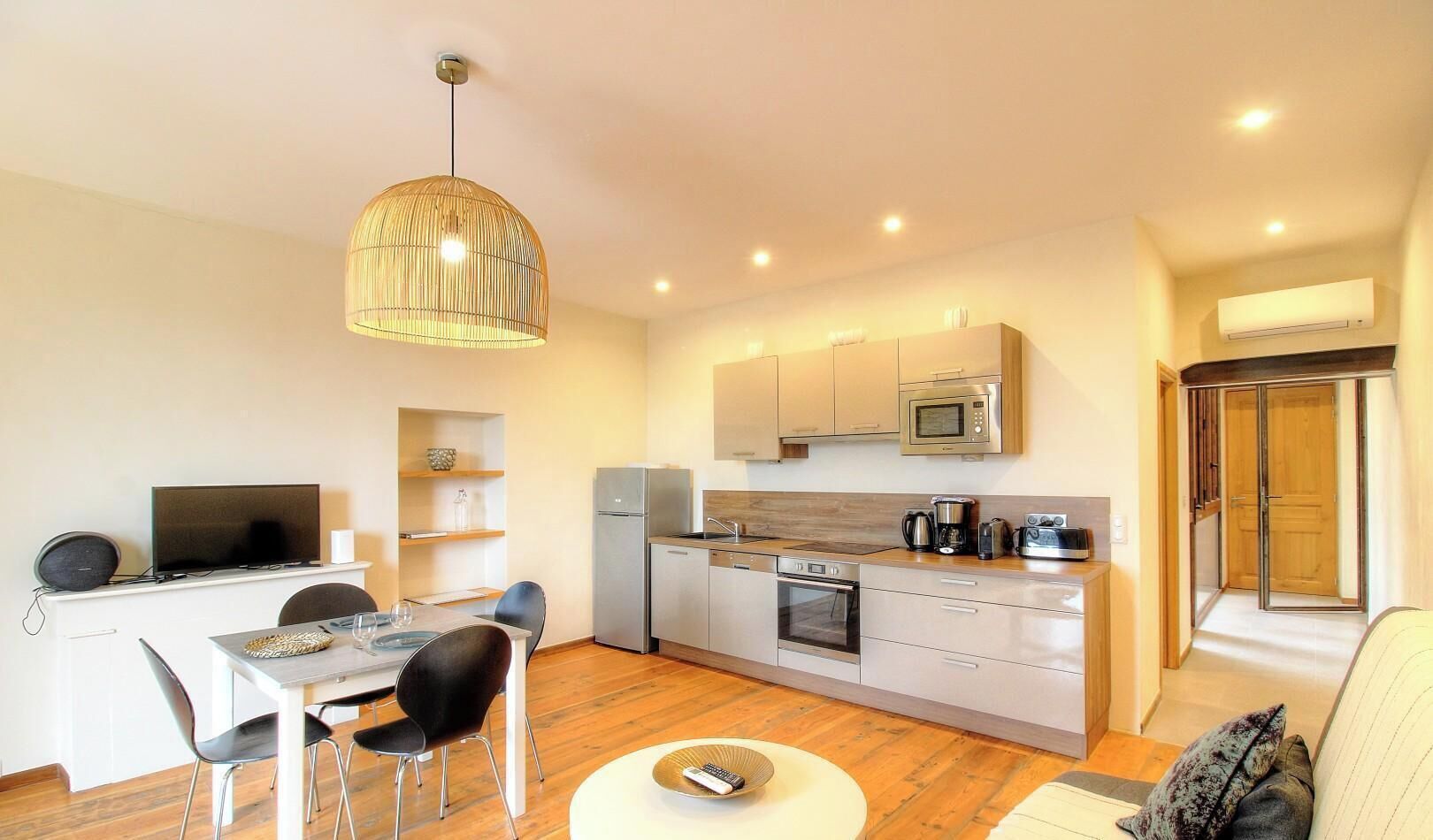 Une cuisine compacte dotée d’appareils électroménagers modernes, un coin repas avec une table et des chaises, et un grand luminaire suspendu.