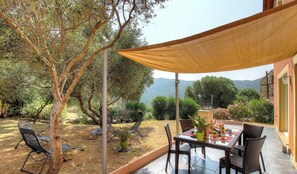 An outdoor patio with a table and chairs, surrounded by trees and a view of the mountains. - Aja puzzuta - COTI CHIAVARI (COTI CHIAVARI)