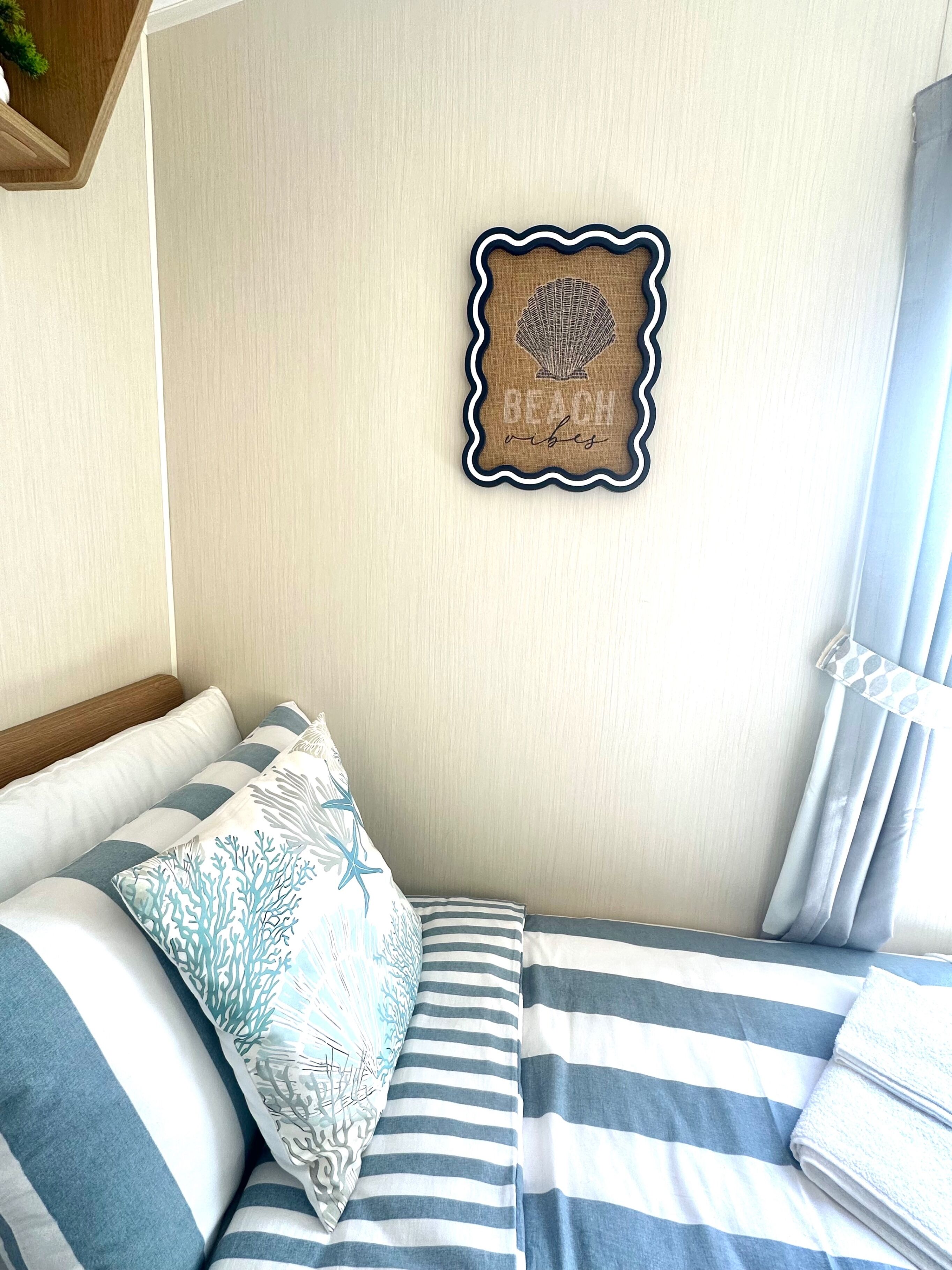 A bed with striped bedding, a decorative pillow, and a wall-mounted piece with a scalloped edge.