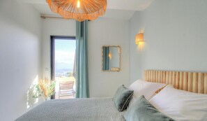 Ein Schlafzimmer mit einem Bett, einem Spiegel, einer Wandleuchte und Blick durch eine Tür.