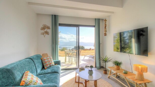 Ein Wohnzimmer mit einer Couch, einem Fernseher, einem Tisch und Blick ins Freie.