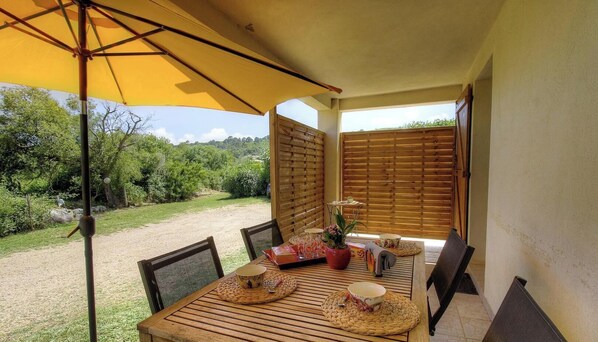 Ein Holztisch mit Stühlen, ein gelber Sonnenschirm und Blick auf einen Garten.