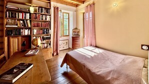 A cozy room with a wooden ceiling, a bookshelf, a desk with a book, a bed, and a window with curtains. - Vacations with family and friends in the countryside (ECCICA SUARELLA)