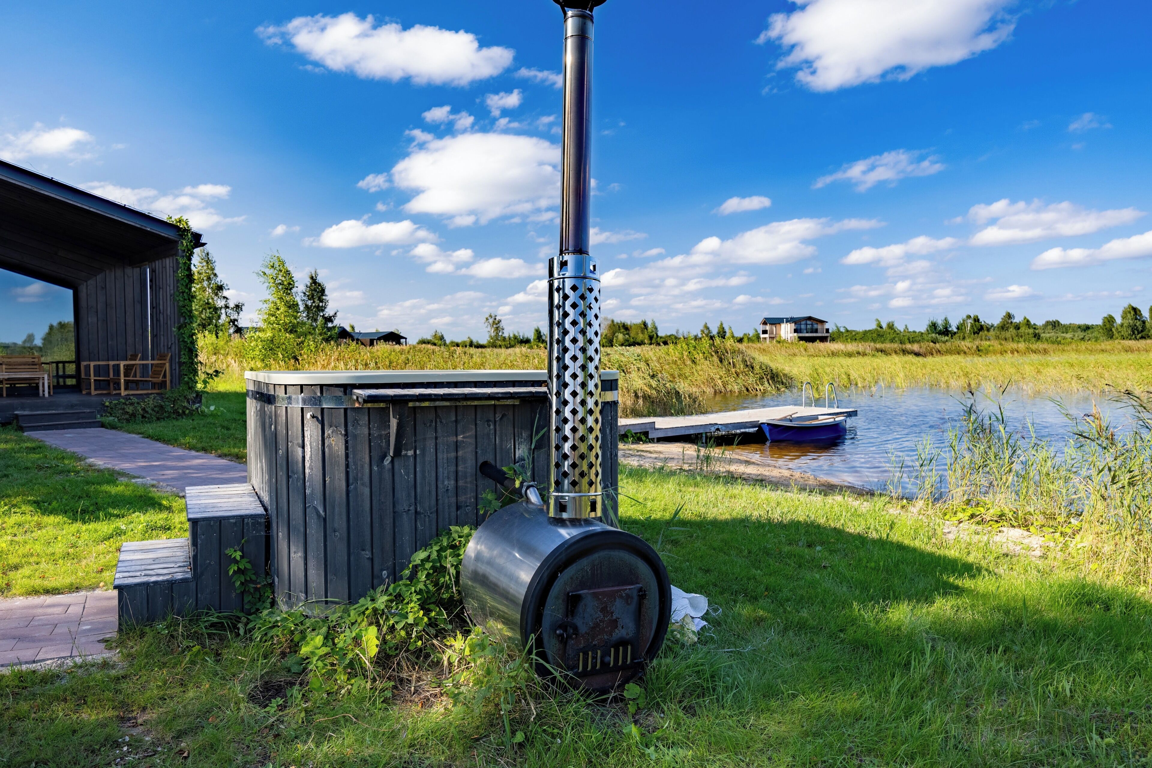 A rustic outdoor setting with a metal stove, wooden shed, and a dock by a calm body of water.
