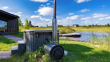 A rustic outdoor setting with a metal stove, wooden shed, and a dock by a calm body of water.