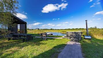 A riverside picnic area with a covered seating area, a hot tub, and a pathway leading to a dock.