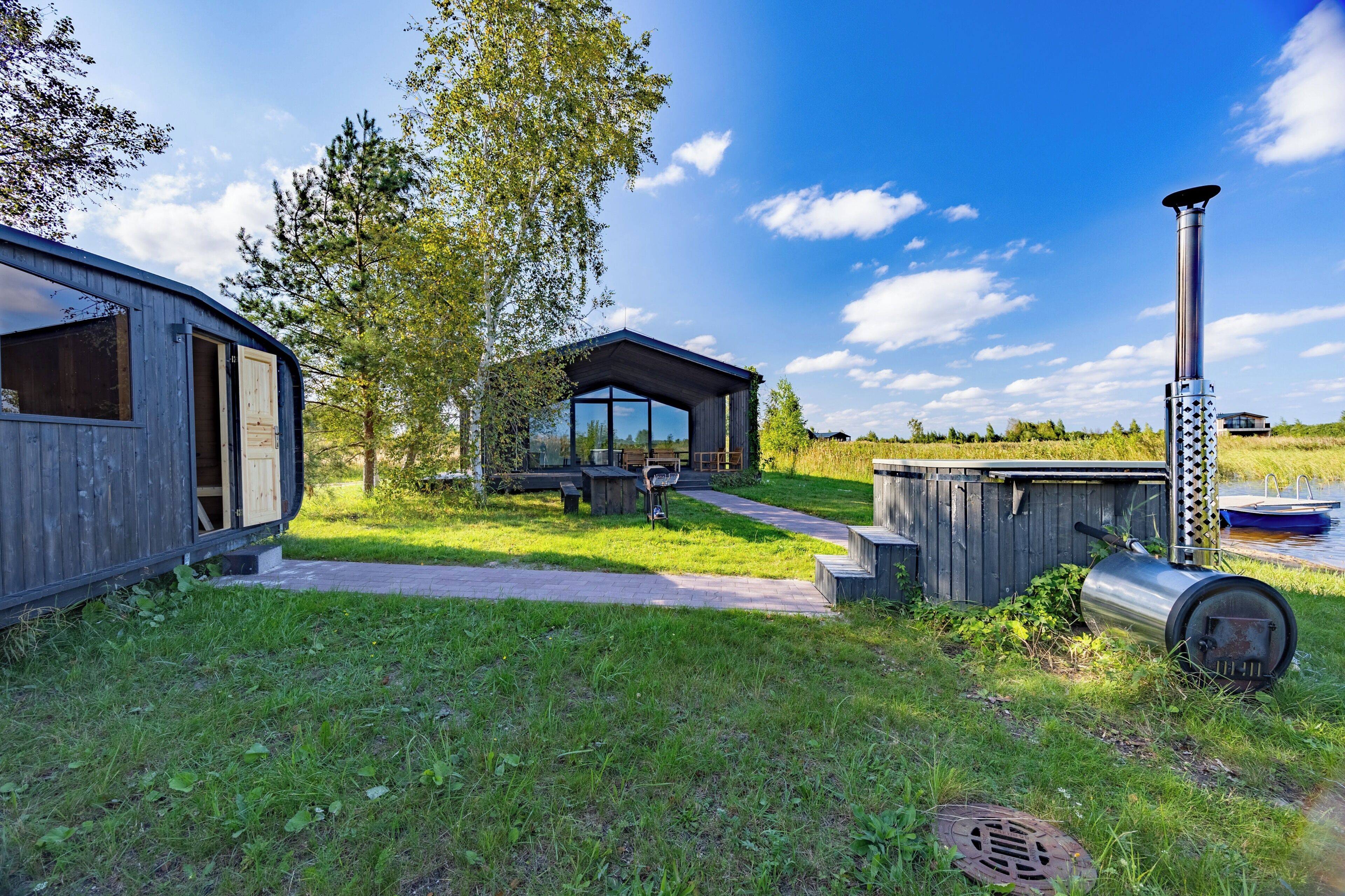 A modern outdoor cabin with a wooden deck, a barbecue grill, and a large window overlooking a grassy area.