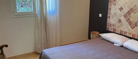 Un dormitorio con cama, ventana con cortinas, mesita de noche y lámpara de pared.