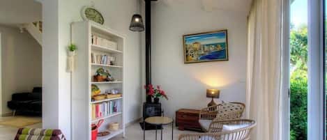 Una sala de estar acogedora con una estantería, un cuadro, muebles de mimbre y vistas a través de una ventana.