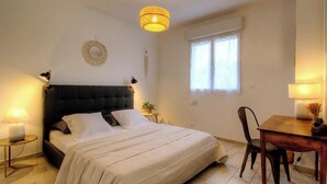 A bedroom with a bed, bedside lamps, a round wall decoration, a window with curtains, and a wooden table with a chair. - CasaNina - BORGO - Guest house (BORGO)