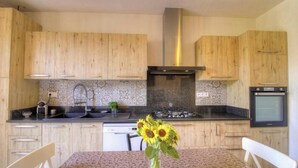 A kitchen with wooden cabinets, a stainless steel range hood, a tiled backsplash, and a dining area with a table and chairs. - Casa Baghjuccia - CARGESE (CARGESE)