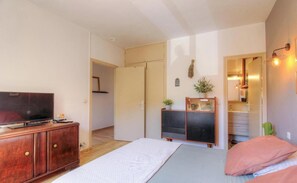 Ein Schlafzimmer mit einem Bett, einem Fernseher auf einer Holzkommode, einem Schminktisch, einer kleinen Pflanze und einem Spiegel.