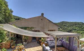 Ein Haus mit einer großen Terrasse, Sitzgelegenheiten im Freien und Blick auf die umliegenden Hügel.