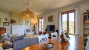 A cozy living room with a wooden dining table, a sofa, a TV, and a balcony with a view. - Casa Baghjuccia - CARGESE (CARGESE)
