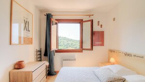 A bedroom with a bed, a window with curtains, a bedside table, a dresser, and a wall-mounted shelf. - Casa Baghjuccia - CARGESE (CARGESE)