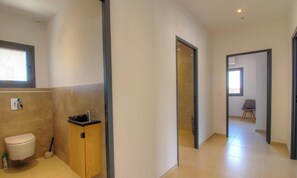 Ein modernes Badezimmer mit Toilette, Waschbecken und Duschbereich. Ein Flur führt zu einem weiteren Raum mit einem Sessel.