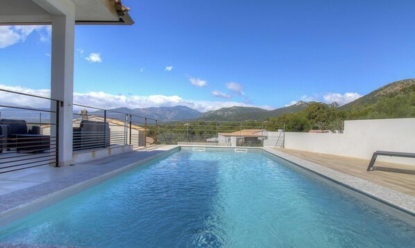 Una piscina con vistas a las montañas, una pared blanca y una barandilla de metal.
