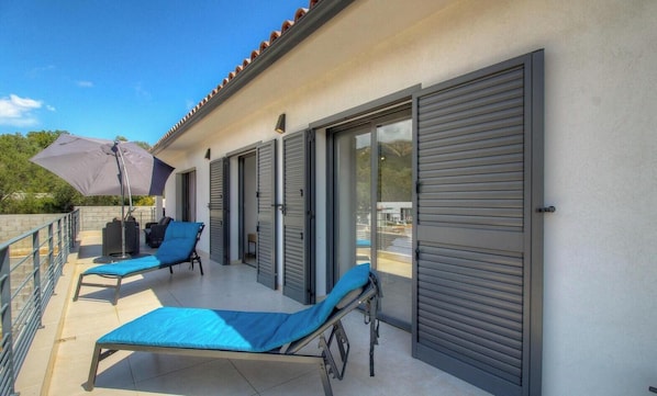 Ein Balkon mit zwei Liegestühlen, einem Tisch und einem Sonnenschirm.