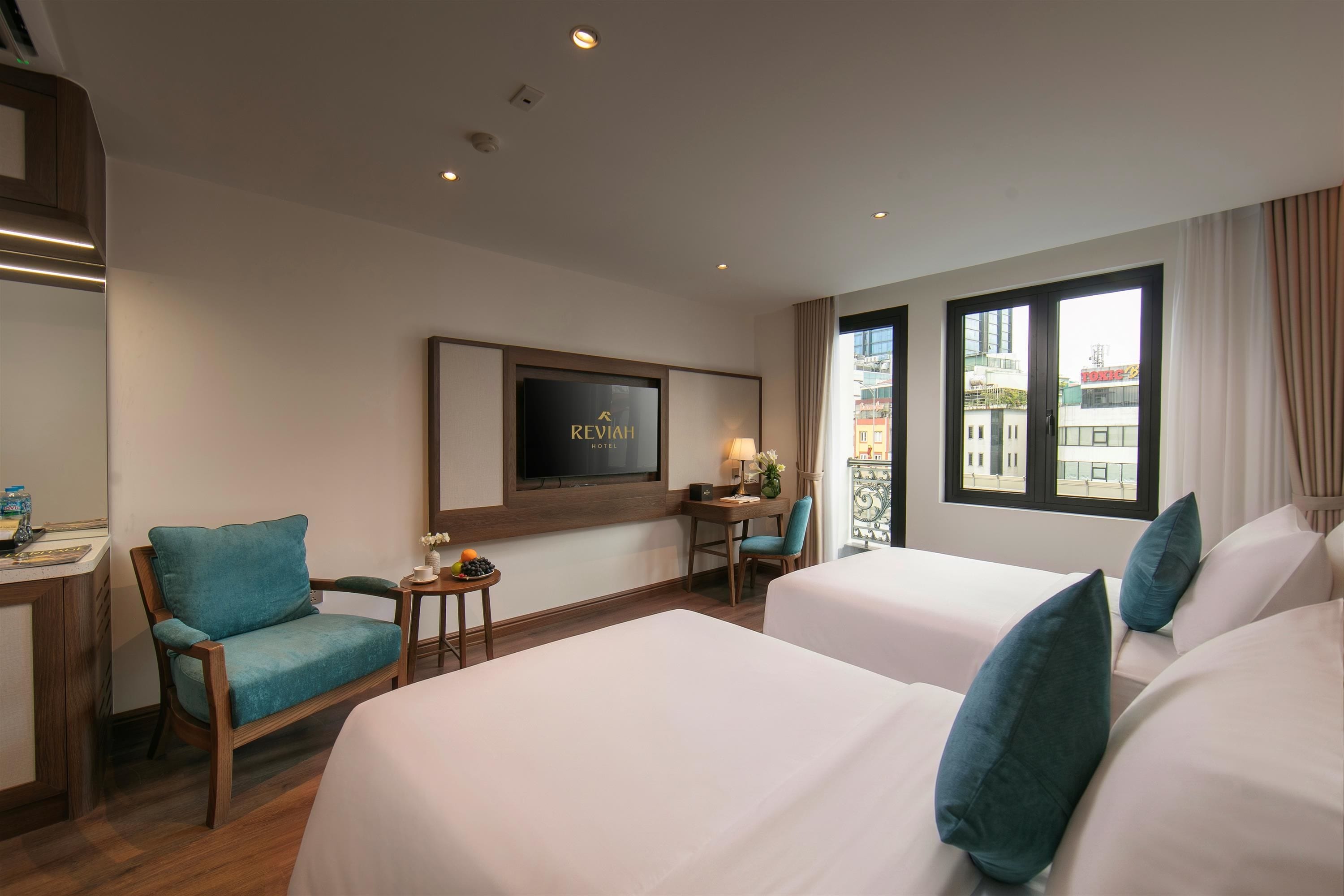 Habitación de hotel con dos camas, un escritorio, una silla, televisión y ventana con vistas a edificios.