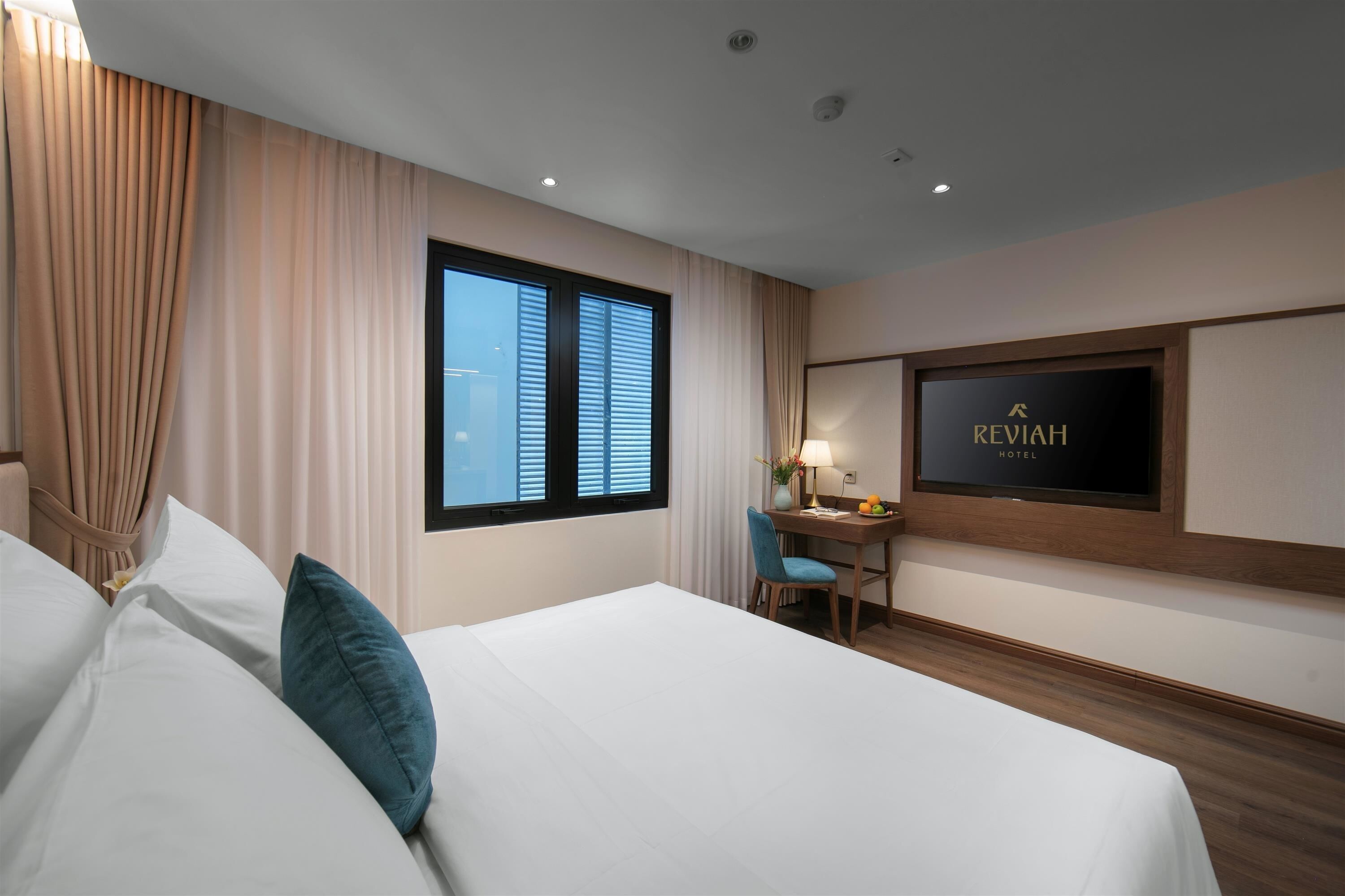 A hotel room with a bed, a desk, a chair, a TV, and a window with curtains.