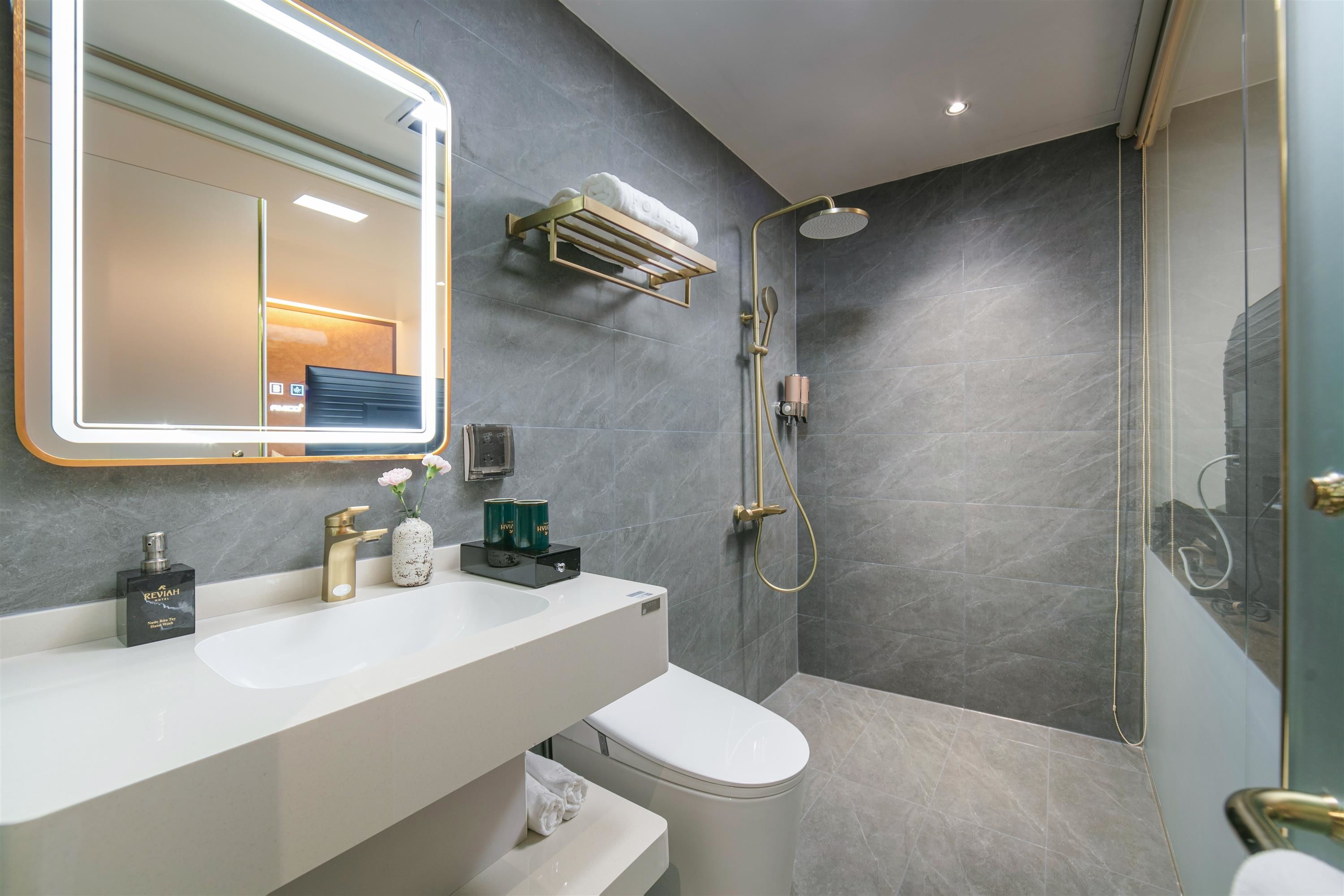 Un baño moderno con un espejo grande, un tocador con lavamanos, un inodoro y una zona de ducha.
