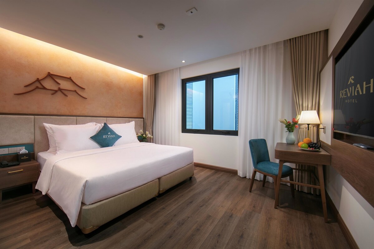 Een hotelkamer met een bed, een bureau, een stoel, een nachtkastje, een televisie en een raam met gordijnen.