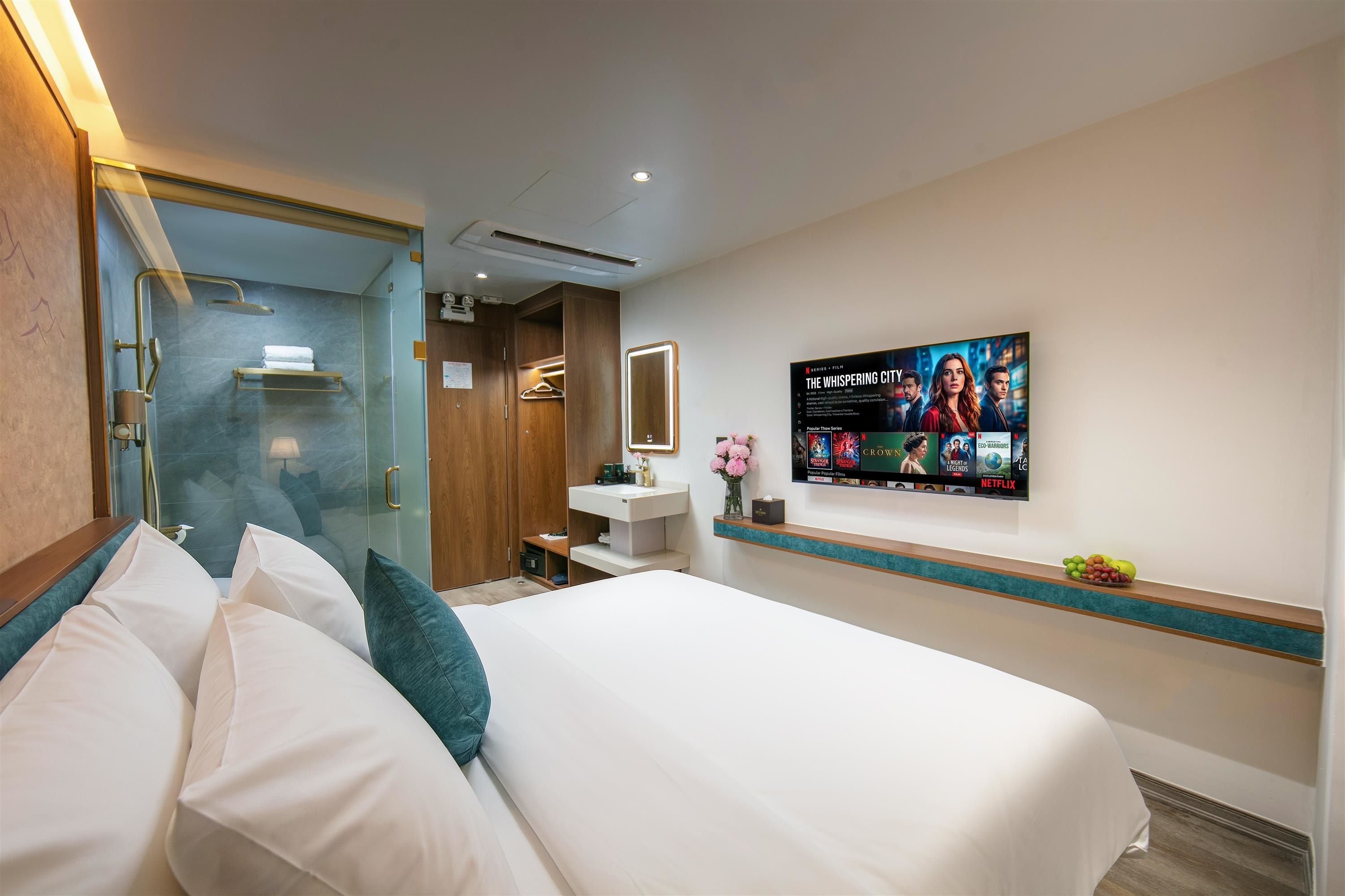 A hotel room with a bed, a bathroom, a vanity, and a wall-mounted TV displaying a movie.