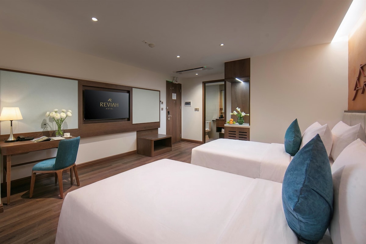 Een hotelkamer met twee bedden, een bureau met stoel, een televisie en een spiegel.