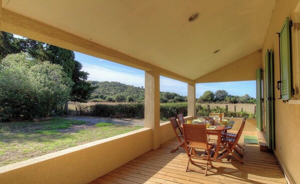 Eine überdachte Terrasse mit Tisch und Stühlen, mit Blick auf einen Garten und eine hügelige Landschaft.