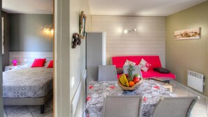 Una habitación con una cama, una mesa de comedor con sillas, un sofá rojo y una cesta de frutas.