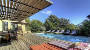 Ein Poolbereich mit Holzterrasse, Liegestühlen und einer überdachten Lounge.