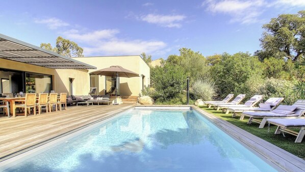 En swimmingpool med solstolar, ett trädäck och en byggnad med en pergola.