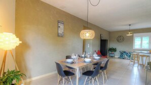 A dining area with a table set for four, a hanging light fixture, and a clock on the wall. - Calm - VIGGIANELLO - Gîte (VIGGIANELLO)