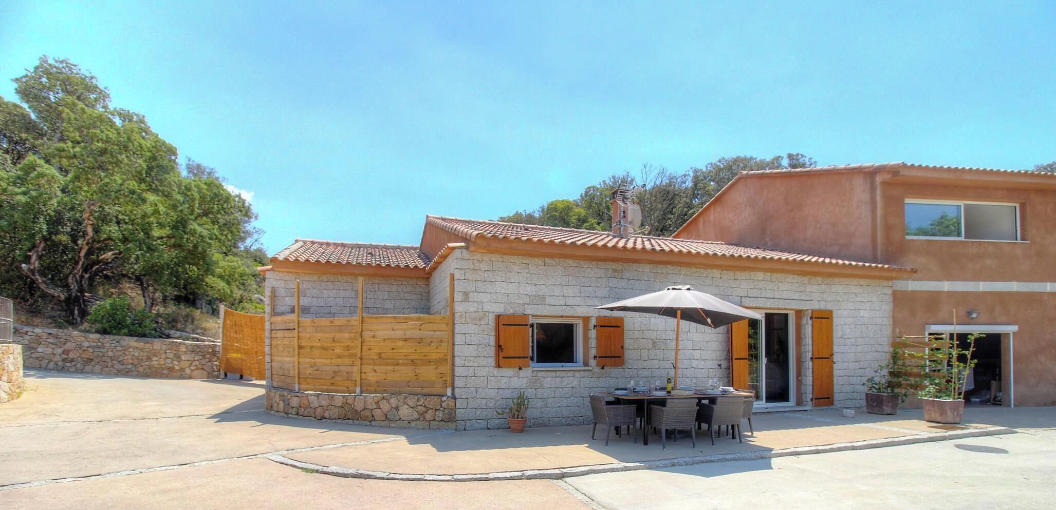 A two-story house with a stone facade, wooden shutters, and a patio with outdoor furniture.