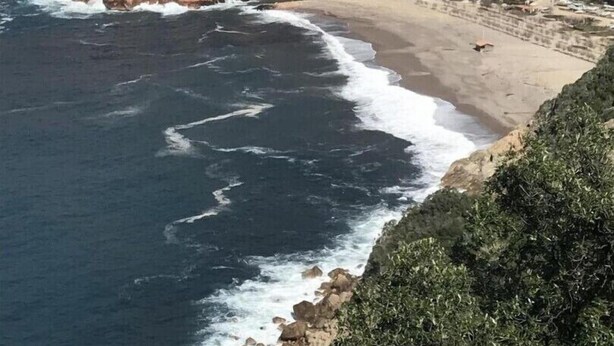 Ein Küstenort mit Gebäuden direkt am Strand, felsigen Klippen und Blick auf das Meer.