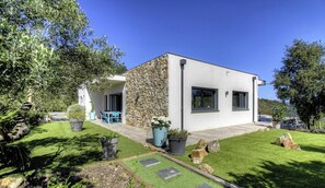 Ein modernes Haus mit Naturstein-Fassade, einer Terrasse mit Gartenmöbeln und einem gepflegten Garten.