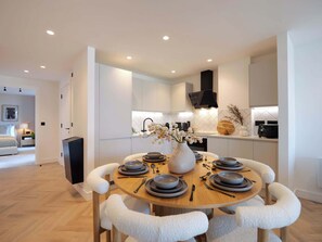 A modern kitchen with white cabinetry, a dining table set for four, and a central vase with flowers. - The Marengo at The Heim (Greater Manchester)