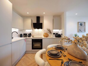 A modern kitchen with white cabinetry, a built-in oven, and a dining area with a round table set for four. - The Marengo at The Heim (Greater Manchester)