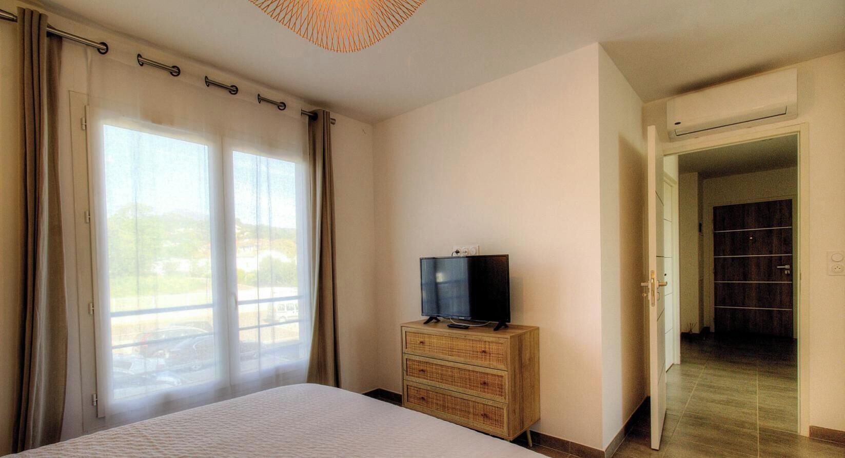 Una camera da letto con un letto, una televisione su una cassettiera in legno e vista dalla finestra.