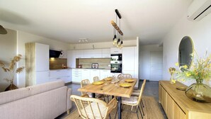 A modern kitchen with white cabinets, a wooden dining table, wicker chairs, and a built-in oven. - Le Figuier - FOLELLI (FOLELLI)