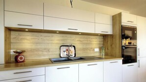 A modern kitchen with a wooden backsplash, stainless steel appliances, and white cabinetry. - Le Figuier - FOLELLI (FOLELLI)