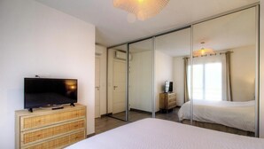 A hotel room with a bed, a television on a wooden dresser, a mirror, and a sliding door closet. - Le Figuier - FOLELLI (FOLELLI)