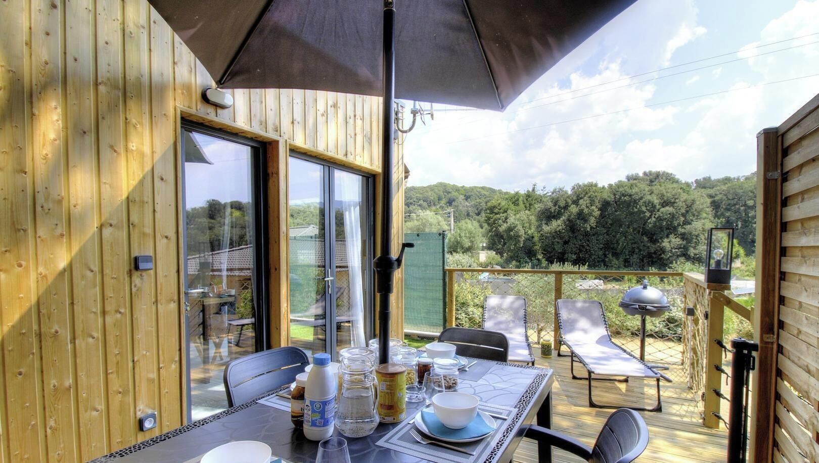 A wooden deck with a table set for dining, outdoor chairs, and a grill.