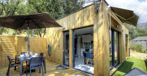 Eine Holzhütte mit Essbereich, Küche und einer Terrasse mit Sonnenschirm.