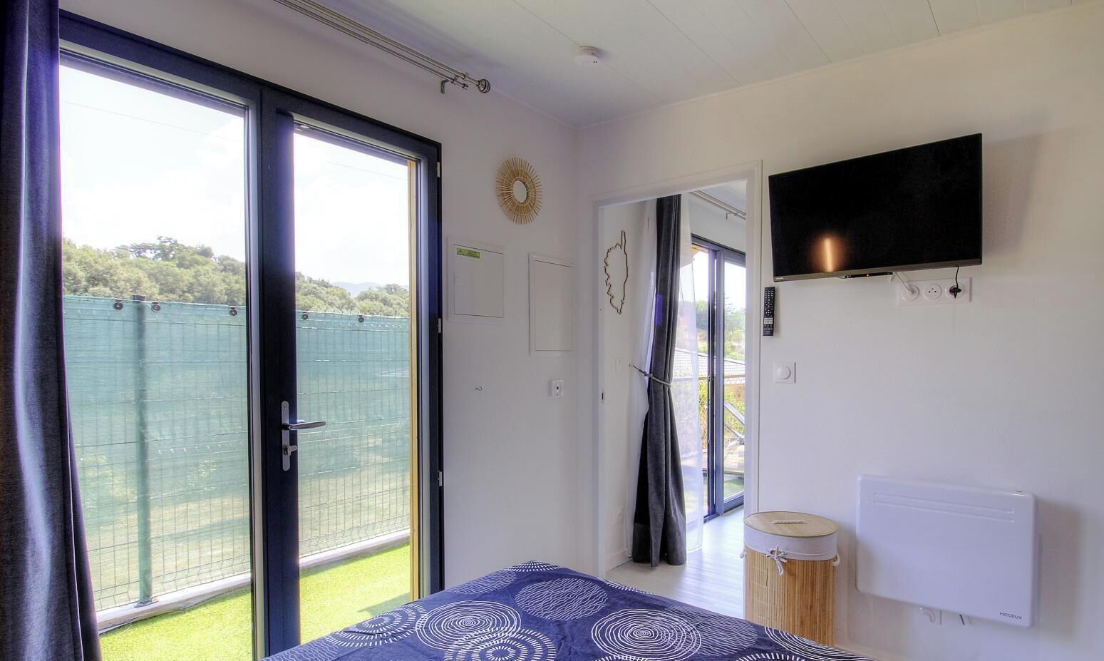 Une chambre avec un lit, une télévision, un radiateur et une porte-fenêtre coulissante donnant sur un espace extérieur.