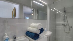 A modern bathroom with a glass shower enclosure, a sink with a mirror, and a stack of towels. - Villa Loulou - BONIFACIO (BONIFACIO)