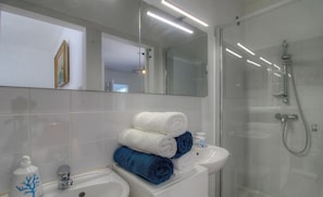 Ein modernes Badezimmer mit Duschkabine aus Glas, einem Waschbecken mit Spiegel und gestapelten Handtüchern.