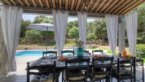 A covered outdoor dining area with a pool view, wooden tables, and chairs. - Villa Loulou - BONIFACIO (BONIFACIO)